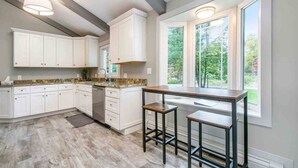 A modern kitchen with white cabinets, a granite countertop, and a window with a view of greenery.