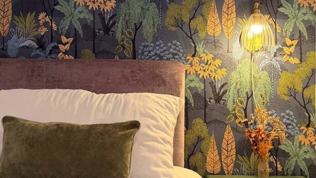 Ein Schlafzimmer mit gestreifter Tapete, einem Bett mit Kissen und einem Nachttisch mit Lampe.