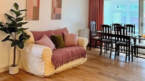 Ein Wohnzimmer mit einer Couch, einem Esstisch mit Stühlen, einer Topfpflanze und abstrakter Wandgestaltung.