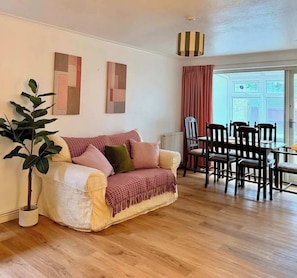 Un salon comprenant un canapé, une table à manger avec des chaises, une plante en pot et des œuvres d’art abstraites accrochées au mur.