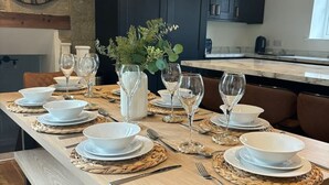 Une table à manger dressée avec de l’assiette blanche, des bols et des verres à vin, entourée de chaises en cuir marron.