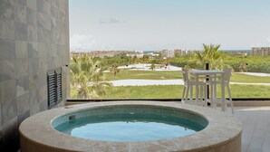 A hot tub in a spacious room with a view of a golf course and buildings.