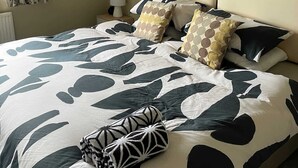 A bed with a geometric patterned bedspread, a round wall hanging, and a wall-mounted lamp. - Spacious Village House near Oxford with Woodburner (Horspath)
