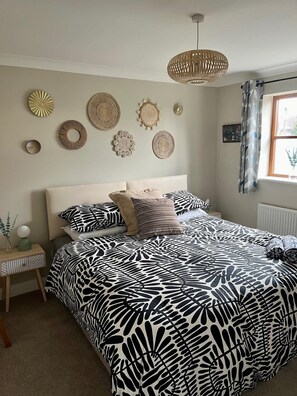 A bedroom with a bed, bedside table, wall decor, and a window with curtains.