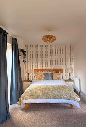 Une chambre à coucher bien rangée, avec un lit, deux tables de chevet, un luminaire suspendu et un papier peint à motifs.