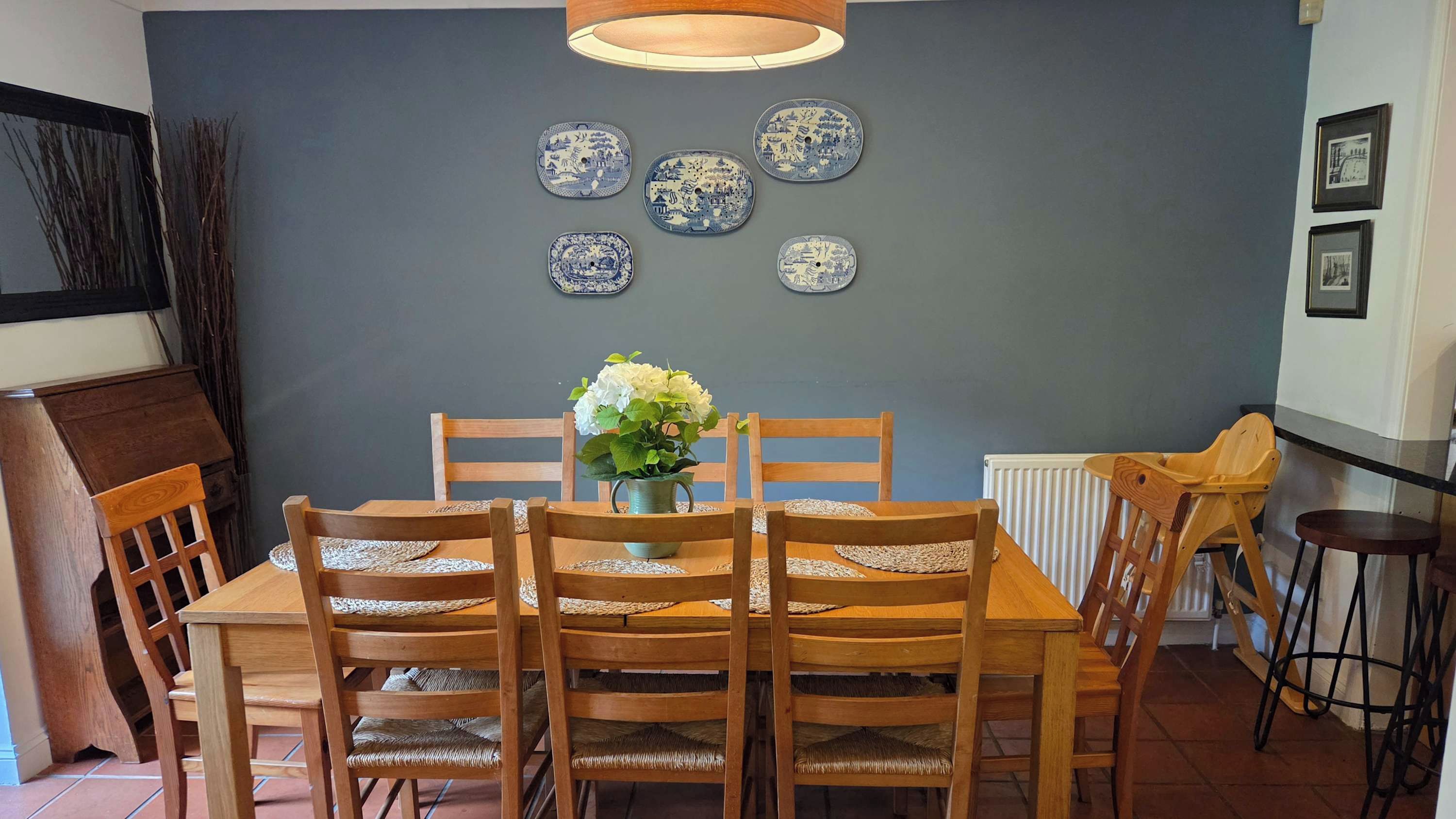 A dining area with a wooden table and chairs, a vase with flowers, and decorative plates on the wall.