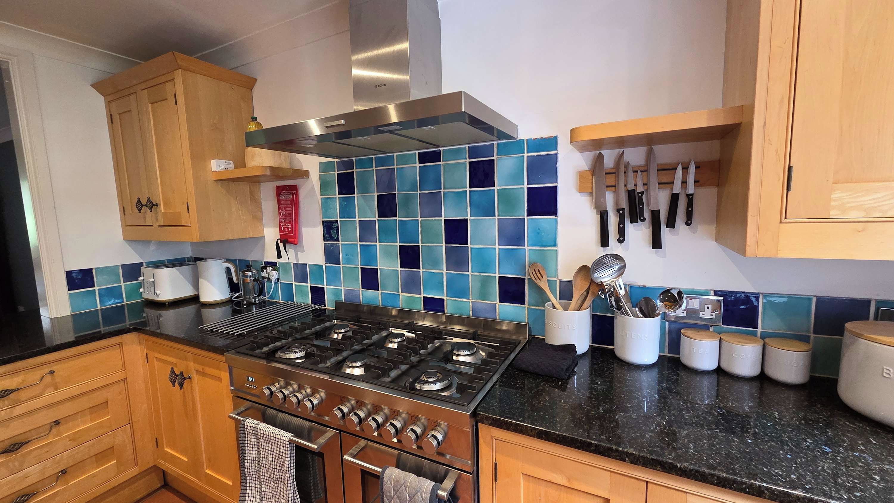A kitchen with wooden cabinets, a gas stove, a coffee maker, and a knife rack.