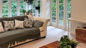 A spacious living room with a large sofa, a wooden coffee table, and a view of greenery through large windows.