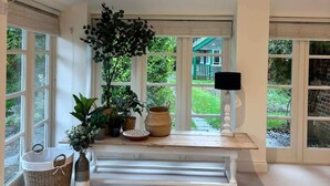 A bright room with large windows, a bench, and various potted plants.