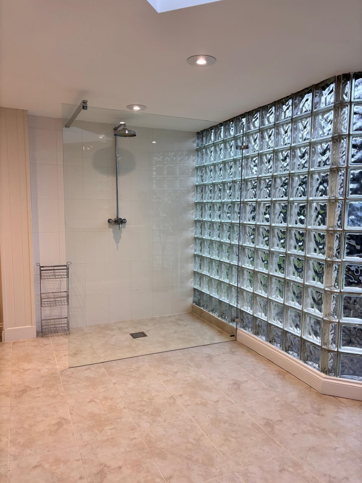 Une salle de bain moderne avec une douche à parois de verre, des murs carrelés et un étagère en métal.
