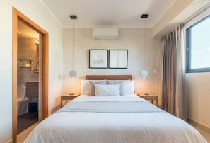 Quarto de hotel com uma cama grande, duas mesas de cabeceira, cabeceira, unidade de ar condicionado e janela com cortinas.