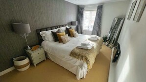 A bedroom with a large bed, bedside tables, a lamp, and a window with curtains.
