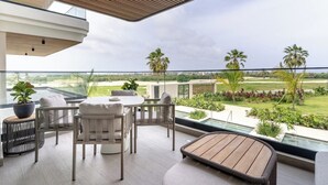 Een modern terras buiten met een houten tafel en stoelen, een comfortabele bank en uitzicht op een golfbaan en groen.