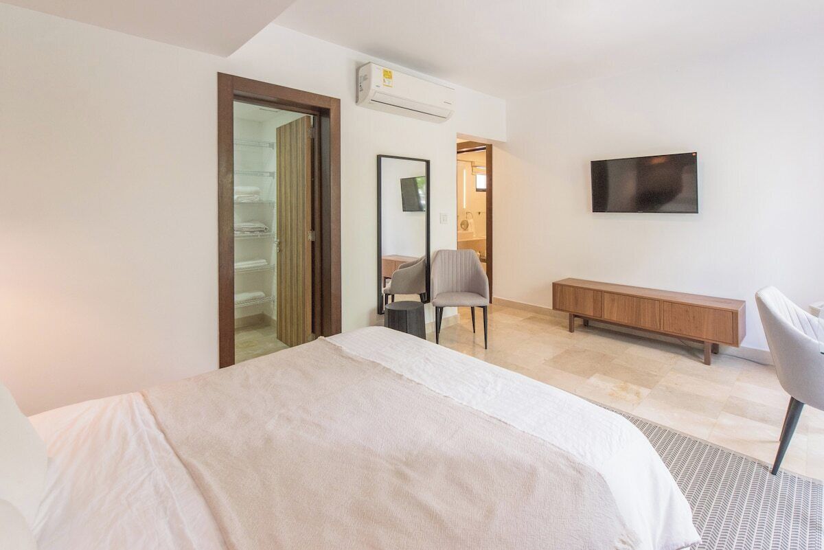 Une chambre d’hôtel avec un lit, un téléviseur fixé au mur, un banc en bois et une chaise.