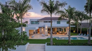 Ein modernes Haus mit Pool, Sitzgelegenheit im Freien und Palmen.