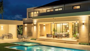 Ein modernes Haus mit Swimmingpool, Sitzgelegenheiten im Freien und einer gut beleuchteten Terrassenfläche.