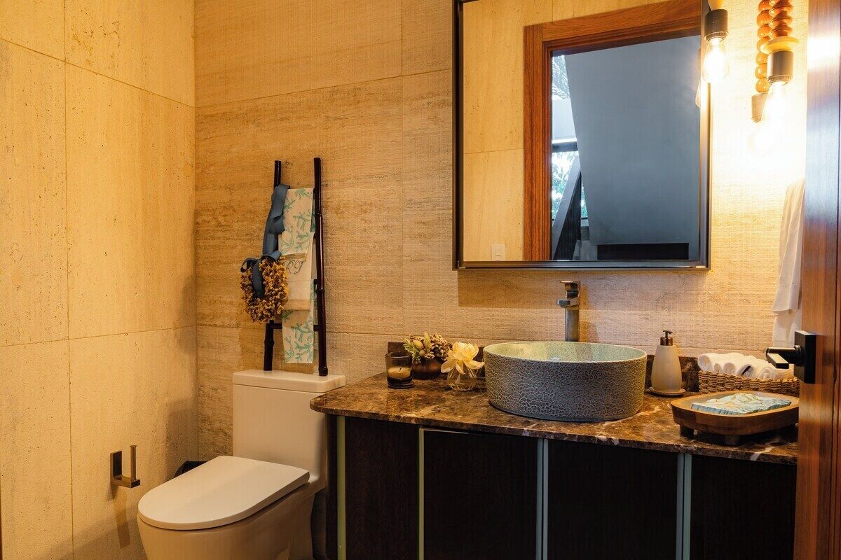 A modern bathroom with a toilet, a sink with a large basin, a mirror, and a wall-mounted light fixture.