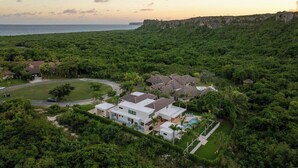 Ein großes, modernes Haus mit mehreren Zimmern und einem Schwimmbad, umgeben von üppiger Vegetation und einer Klippe mit Blick auf den Ozean.