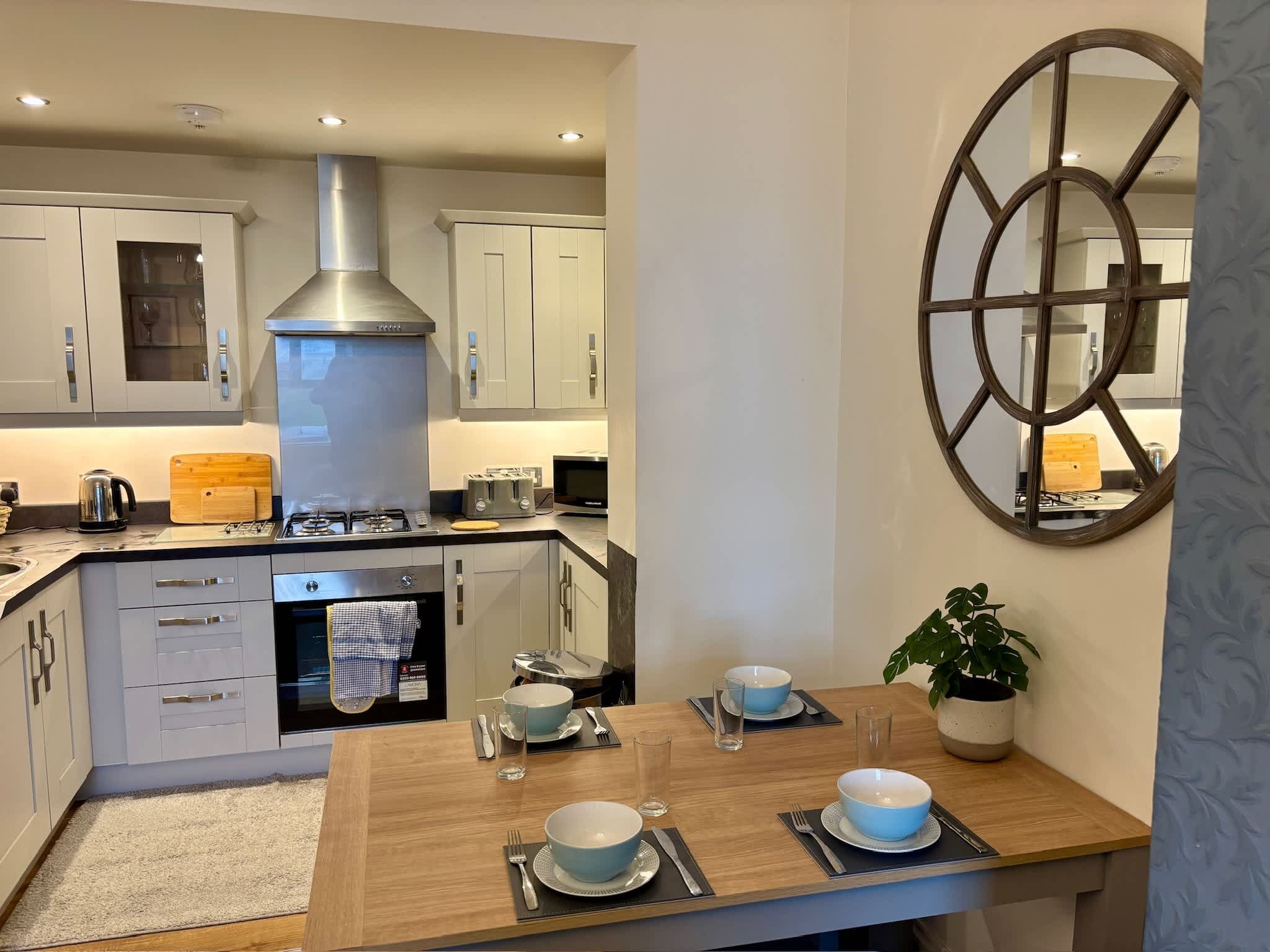 Una cocina moderna con electrodomésticos de acero inoxidable, una campana extractora central y una zona de comedor con una mesa de madera preparada para dos.