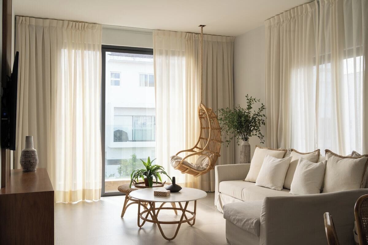 A modern living room with a sofa, a hanging chair, a round table with a vase, and a potted plant.