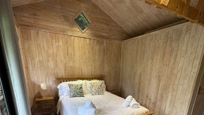 Un dormitorio de madera con una cama, una mesita de noche y una ventana.