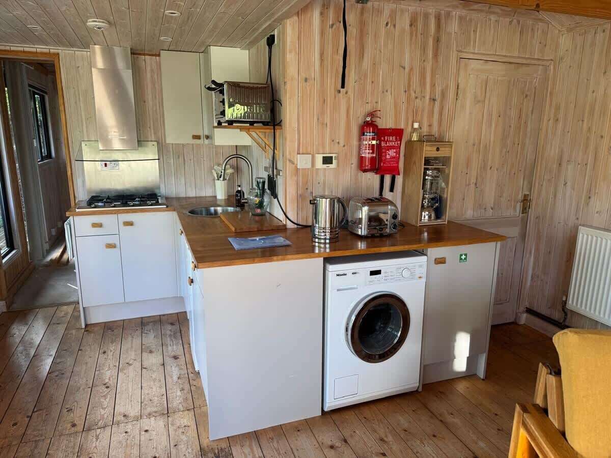 A compact kitchen with a built-in washer and dryer, wooden flooring, and a small dining area.