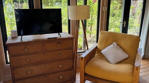 Une commode en bois, un téléviseur à écran plat, une lampe et un coussin à motifs sur une chaise.