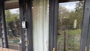Una terraza de madera con un banco y una puerta con un panel de vidrio y una cortina.