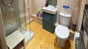 Un baño con paneles de madera, cabina de ducha de vidrio, lavamanos y inodoro.