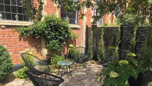 A patio area with outdoor furniture, including chairs and a table, surrounded by potted plants and a brick wall.