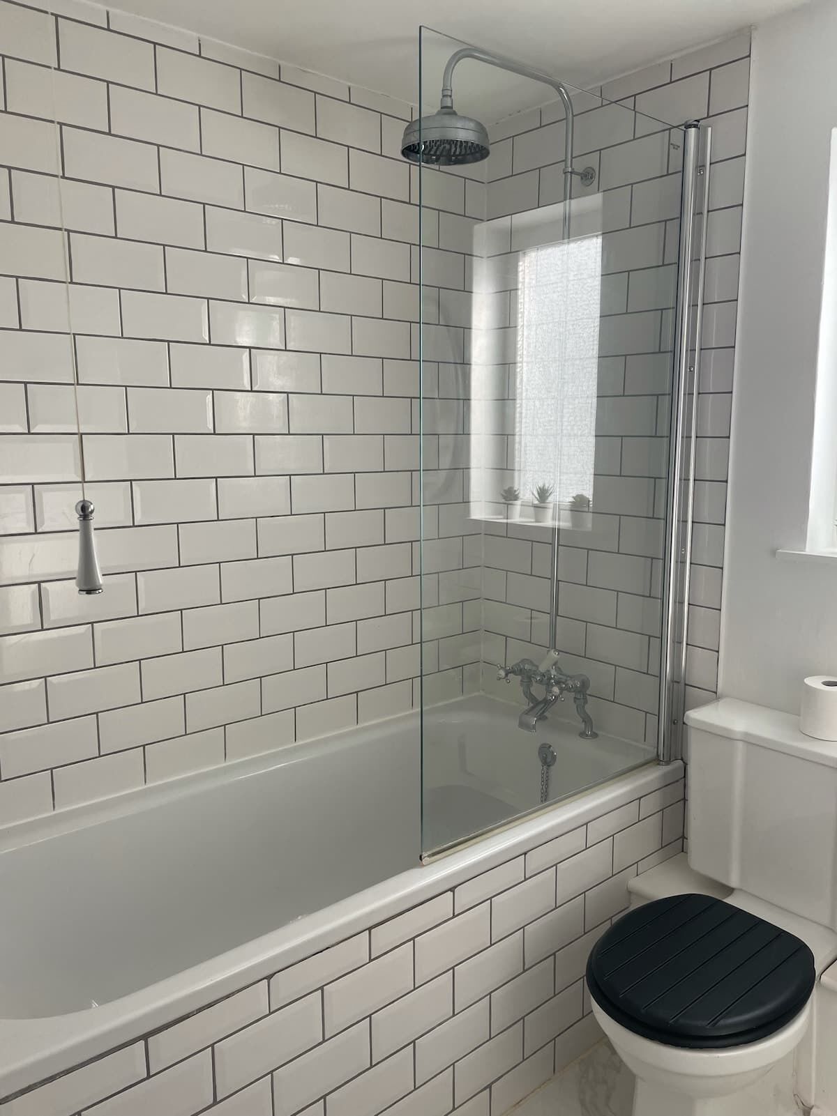 Ett modernt badrum med en dusch som är avskärmad med glasväggar, vita kaklade väggar och en toalett med svart sits.