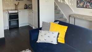 A modern living room with a dark blue sofa, a patterned rug, and a kitchen visible through an archway.