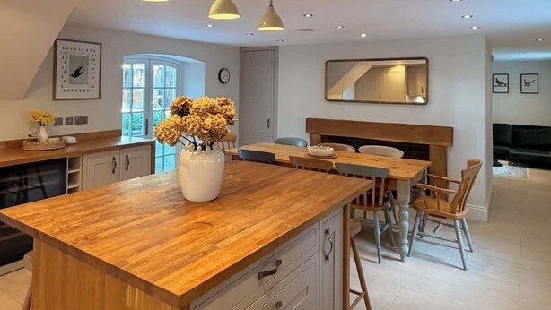 Une cuisine moderne dotée d’un îlot central en bois, de luminaires suspendus et d’un coin repas avec des chaises en bois.