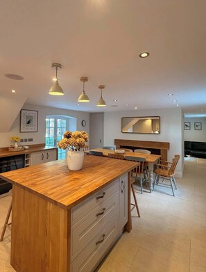 A modern kitchen with a wooden island, pendant lighting, and a dining area with wooden chairs.