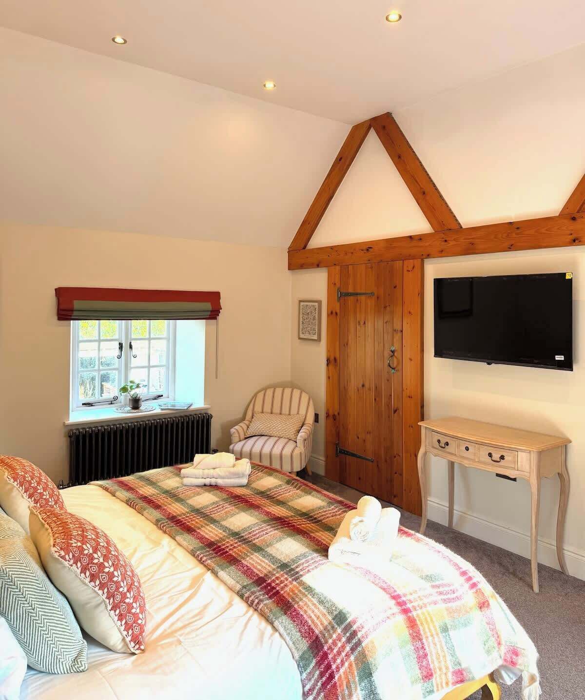 A bedroom with a bed, a chair, a TV, and a window.