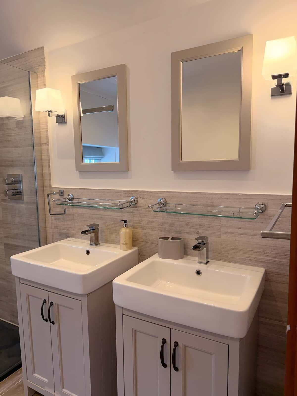 A modern bathroom with two sinks, a mirror, and a glass shelf.