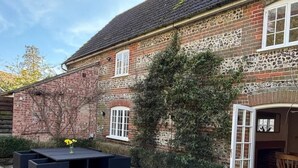 Une maison en briques avec un patio en pierre, un coin repas avec une table et des chaises, et un jardin.