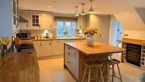 Une cuisine moderne dotée d’un grand îlot central, de plans de travail en bois et de luminaires suspendus.