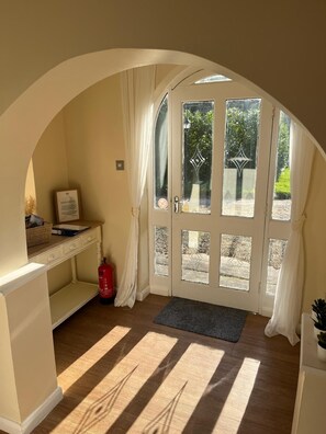 A sunlit room with a wooden floor, a desk with a basket, a framed certificate, and a fire extinguisher. - Walworth Castle Cottage (Darlington)