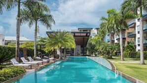 A modern hotel with a swimming pool, palm trees, and a clear sky. - Unique High-End Loft Apt Cap Cana (Ciudad Las Canas, Cap Cana)