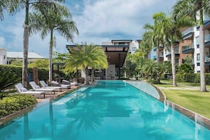 Ein modernes Hotel mit Schwimmbad, umgeben von Palmen und Liegestühlen.