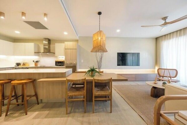 Una cocina moderna con una isla central, sillas de madera y una lámpara colgante.