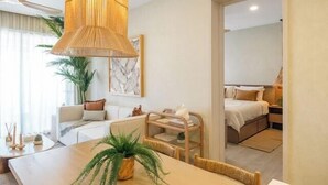 Une chambre d’hôtel moderne dotée d’un coin repas, d’un grand luminaire suspendu et donnant sur la chambre adjacente.