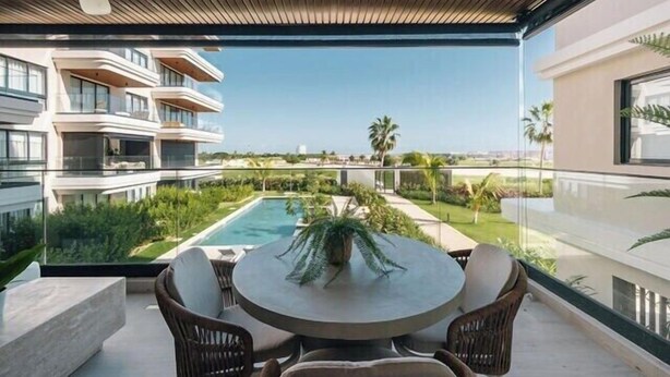 Un espace extérieur moderne, aménagé avec une table ronde et des chaises, offrant une vue sur une piscine et une végétation luxuriante.