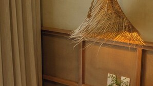 Une chambre confortable avec un luminaire suspendu en fibres tressées, une table de chevet ornée d’un vase et d’une assiette, et un panier en osier rempli de coussins.