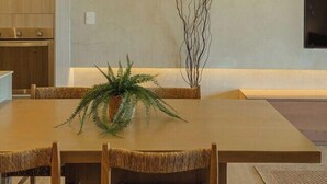 Un espace de salle à manger moderne, avec une grande table en bois, des chaises en osier et un luminaire suspendu en bambou.