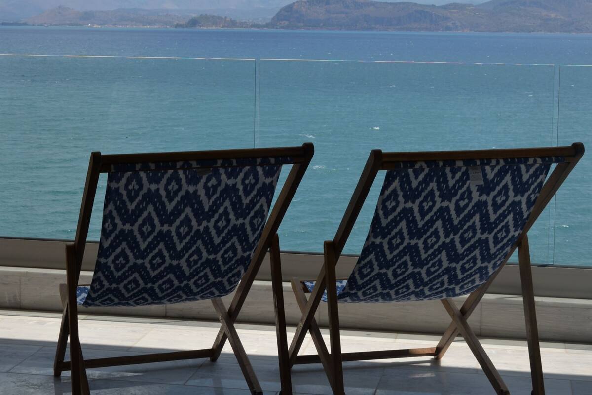 Two folding chairs with a geometric pattern facing a body of water with mountains in the distance.