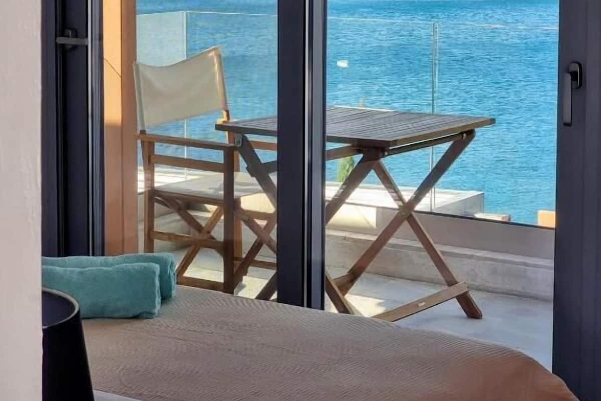 A balcony with a view of the sea, a chair, a table, and a bed.