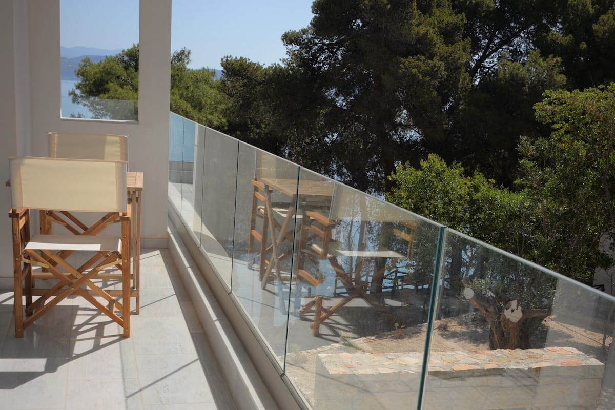 A balcony with a glass railing, wooden chairs, and a view of trees and mountains.