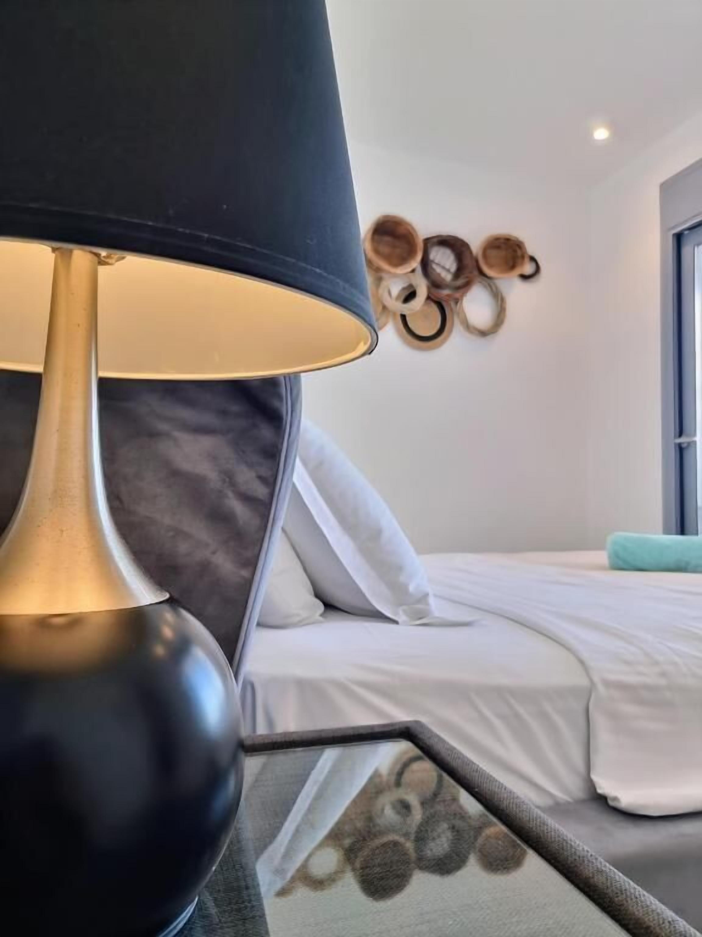 Een bed met wit beddengoed, een zwarte lamp en een wanddecoratie van houten ringen.